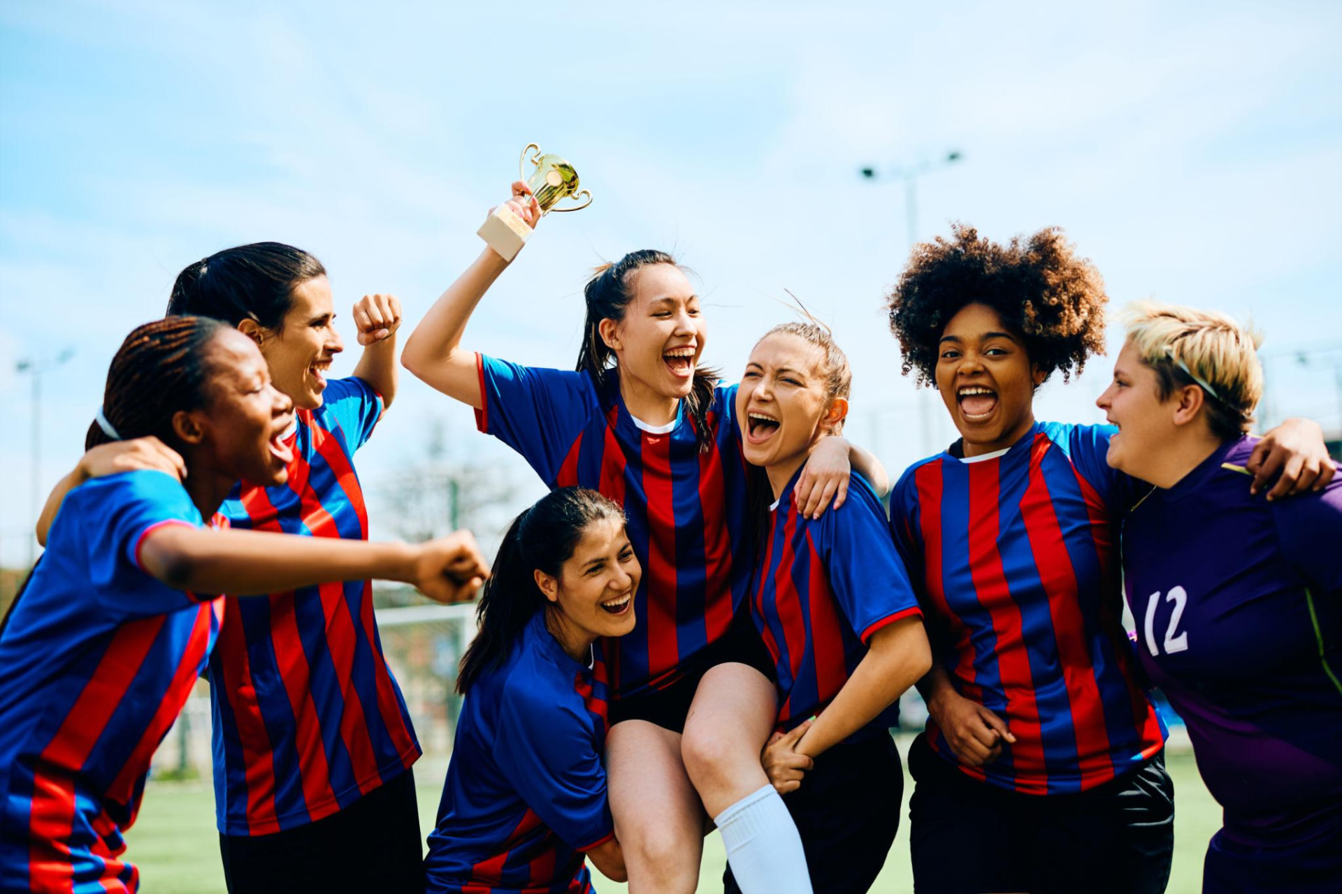 A women's team celebrating together with a trophy on the field